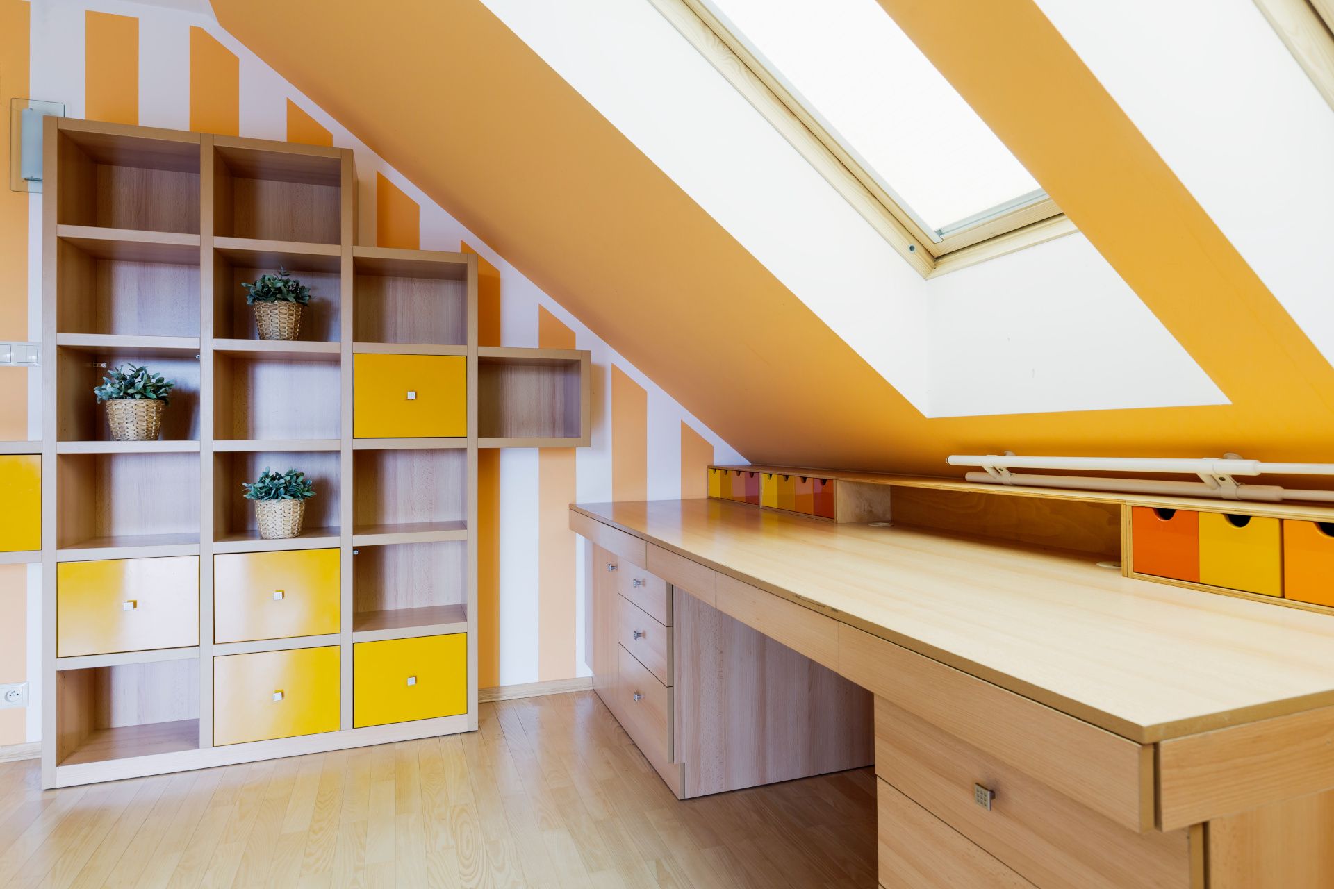 Yellow office room in an attic, with a set of shelves and a long wooden desk